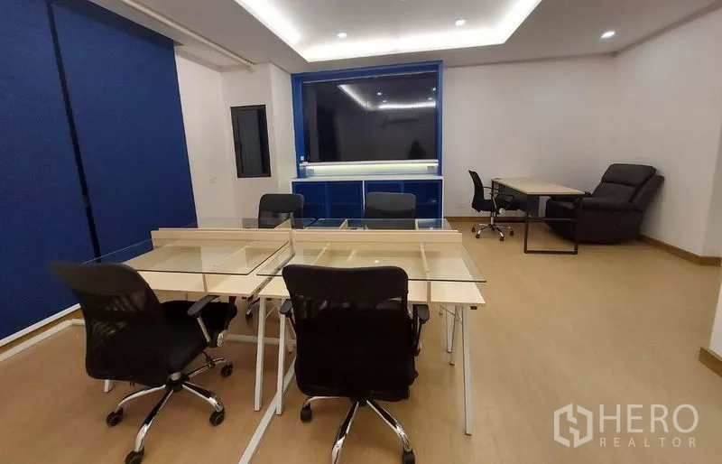 Townhouse for rent in Thanyaburi, Pathum Thani - Office-style workroom with multiple chairs, glass-top desks, and a blue media wall.