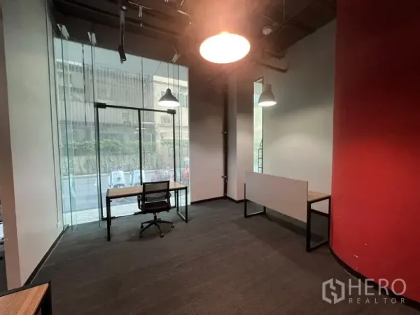 Office Space for rent - Corner workspace with floor-to-ceiling glass, single desk and chair, pendant lights and a red accent wall.