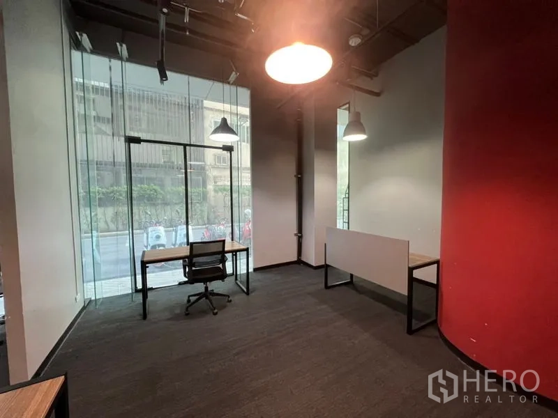 Office Space for rent - Corner workspace with floor-to-ceiling glass, single desk and chair, pendant lights and a red accent wall.