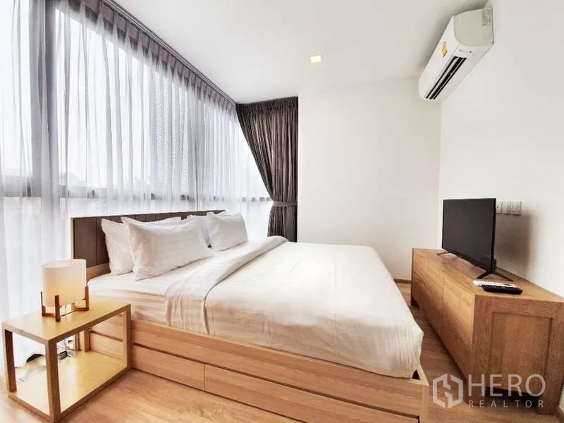 Condominium for sale in Watthana, Bangkok - Master bedroom with king bed, large corner windows, air conditioner and wood furniture.