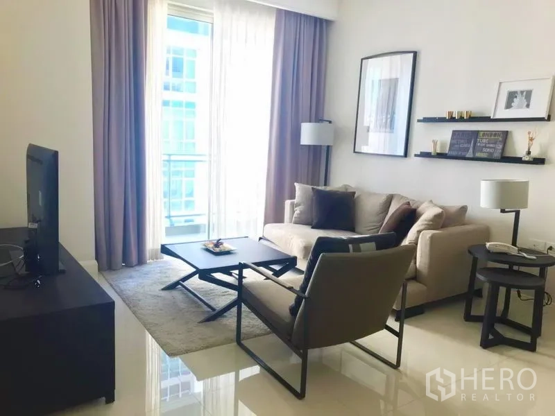 Condominium for rent in Pathum Wan, Bangkok - Bright living room with sofa, armchair, TV unit and a balcony with sheer curtains in a modern Bangkok condo.
