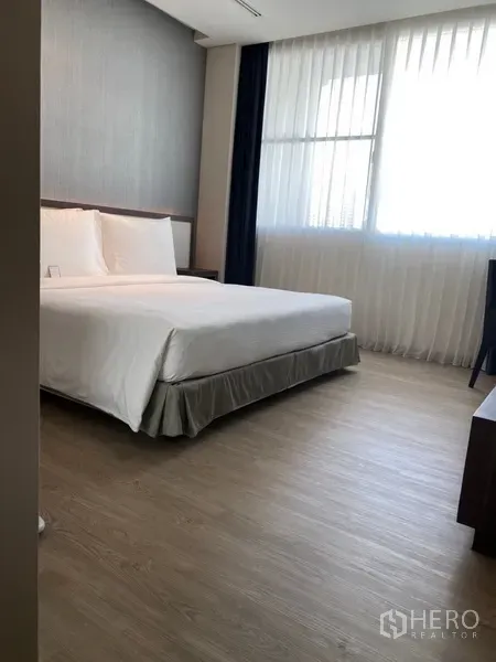 房间 出租在Khlong Toei, Bangkok - 宽敞卧室，配大床、木地板及大窗帘窗户，采光充足。