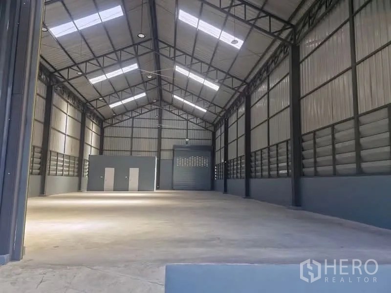 Factory for rent in Khlong Luang, Pathum Thani - Spacious factory hall with high gable roof, steel trusses, skylights, concrete floor and roller shutter.
