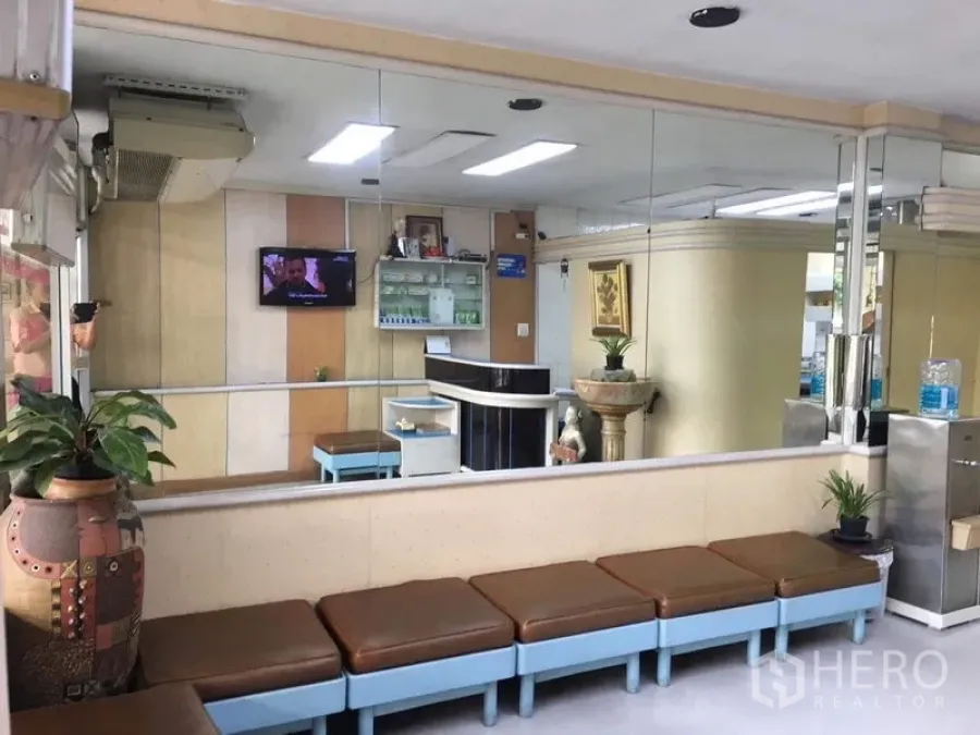 Shophouse for rent in Phra Khanong, Bangkok - Reception area with long bench seating, mirrored wall, plants, and bright ceiling lights.