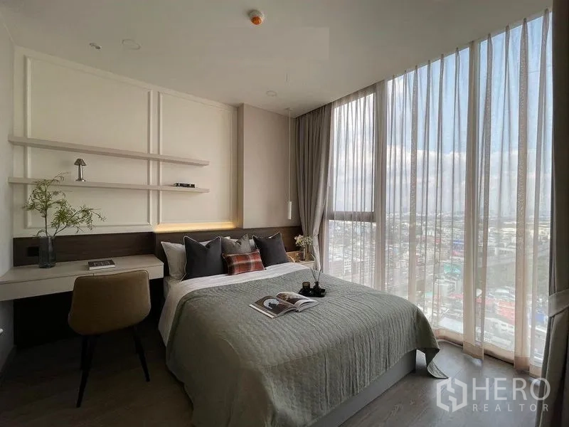 Condominium for rent in Pathum Wan, Bangkok - Bright bedroom with floor-to-ceiling windows, city view, double bed and work desk with shelves.