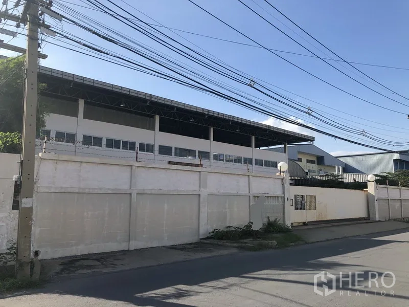 工厂 for sale in Khlong Luang, Pathum Thani - 围墙外观视角，可见厂区与高挑钢结构屋顶。