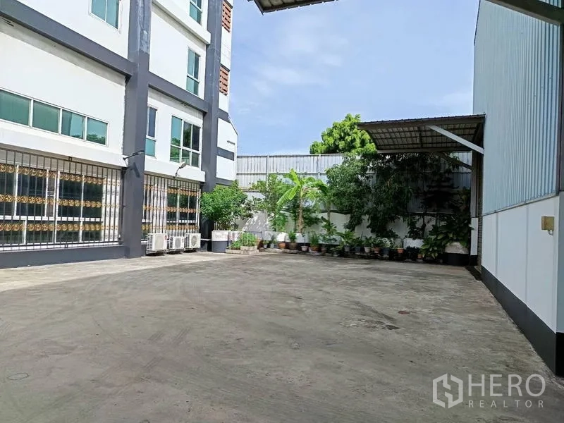 Factory for sale in Ban Phaeo, Samut Sakhon - Office building facade with large windows, AC units and landscaped potted plants in the courtyard.