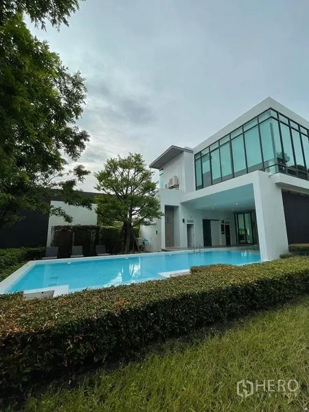 Townhouse for rent in Prawet, Bangkok - Contemporary clubhouse overlooking an outdoor swimming pool and trimmed hedges.