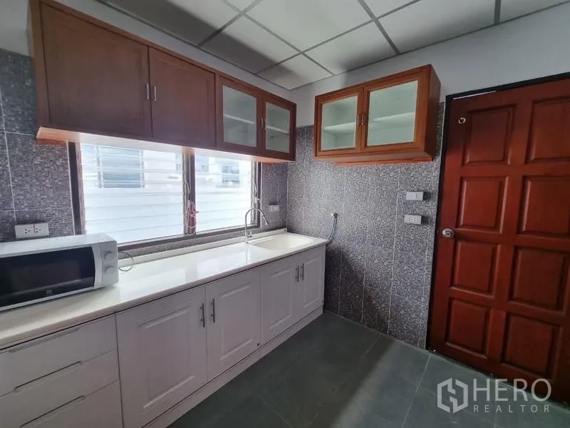 Detached House for rent in Nonthaburi - Fitted kitchen with white countertop, sink, microwave, and upper cabinets.
