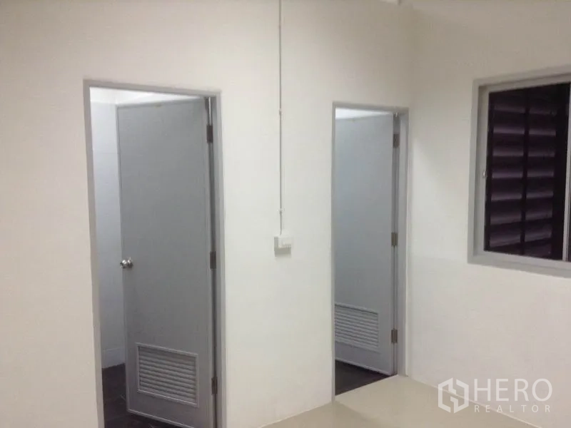 货栈 出租在Bang Kapi, Bangkok - 走廊内有两扇灰色门通往卫生间与杂物间，配百叶窗。