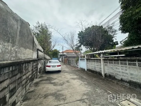 地 出售在Phra Khanong, Bangkok - 狭窄的住宅巷道，沿线高墙与架空电缆，白色轿车停靠路边。