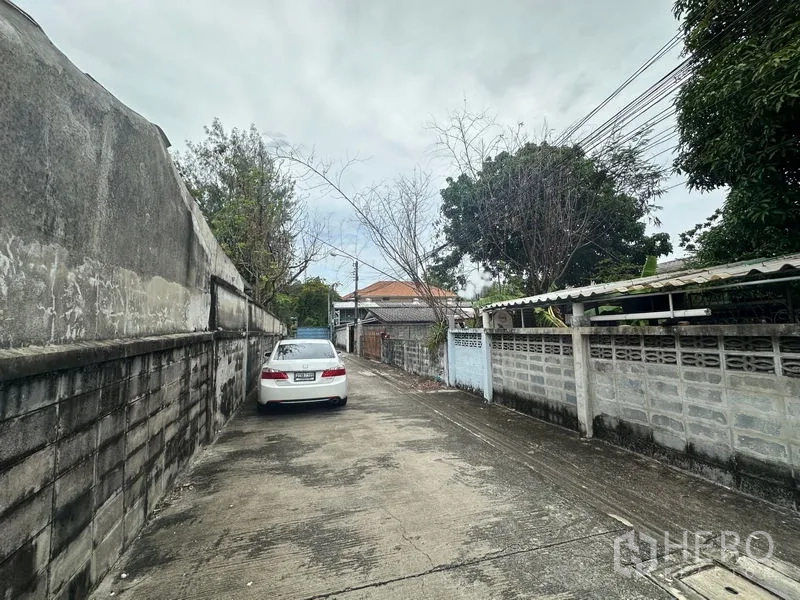 地 出售在Phra Khanong, Bangkok - 狭窄的住宅巷道，沿线高墙与架空电缆，白色轿车停靠路边。