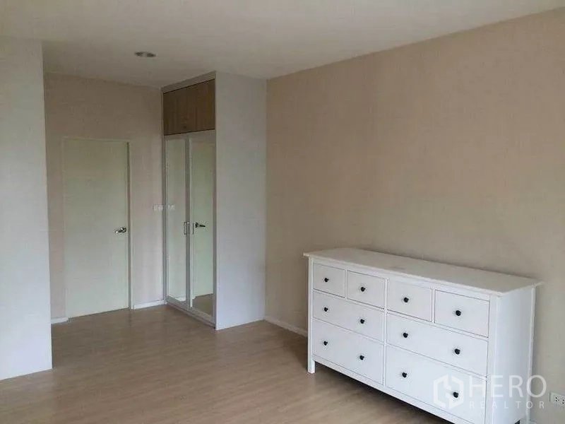 Townhouse for sale in Suan Luang, Bangkok - Spacious bedroom with white dresser and mirrored built-in wardrobe.
