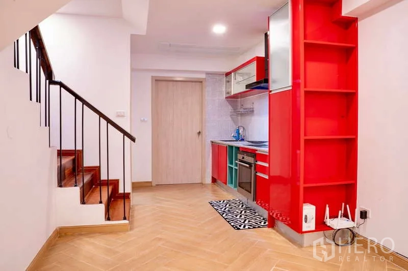 Townhouse for rent in Khlong Toei, Bangkok - Compact kitchen with bold red cabinetry under the stairs and built-in appliances.