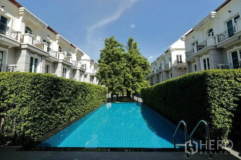 Townhouse for rent in Watthana, Bangkok - Shared swimming pool framed by hedges within the townhouse community.