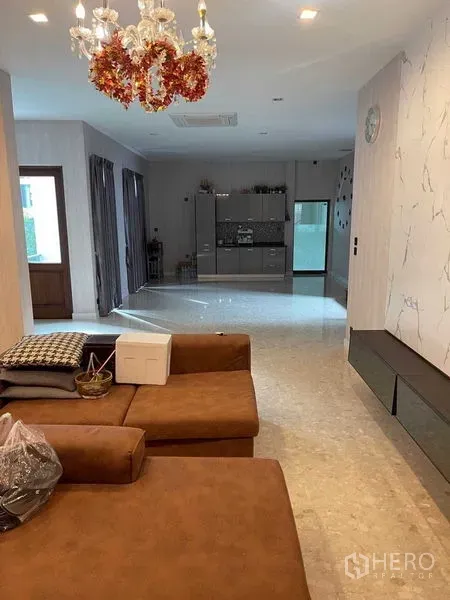 Detached House for sale in Mueang Samut Prakan, Samut Prakan - Open-plan living area with brown sectional sofa, chandelier and view to a modern pantry and glass doors.