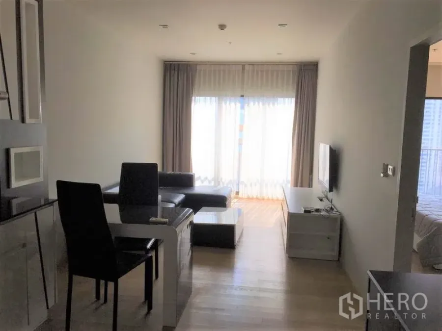 Condominium for rent in Bangkok - Open-plan living and dining area with TV console, dining set and balcony doors, with the bedroom adjoining.