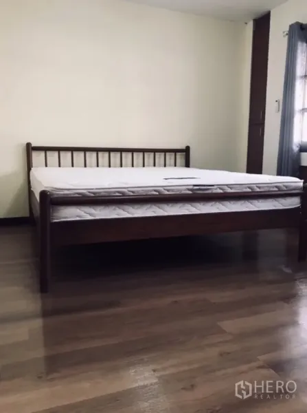 Townhouse for rent in Watthana, Bangkok - Bedroom with wooden bed frame and mattress over polished wood flooring.