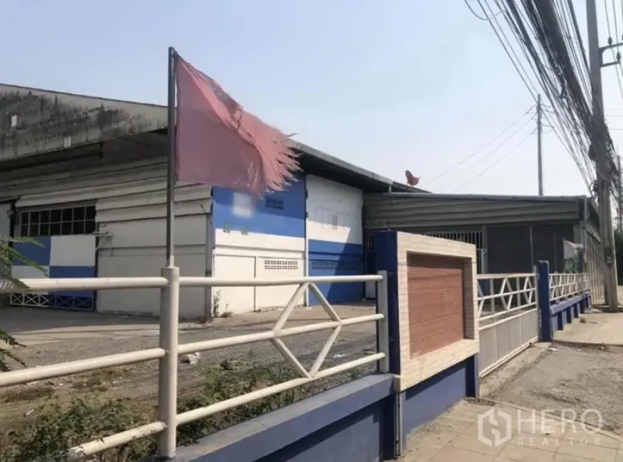 Warehouse for rent in Bang Phli, Samut Prakan - Street-side view of a blue-and-white warehouse with gated fence and overhead power lines in Bang Phli.