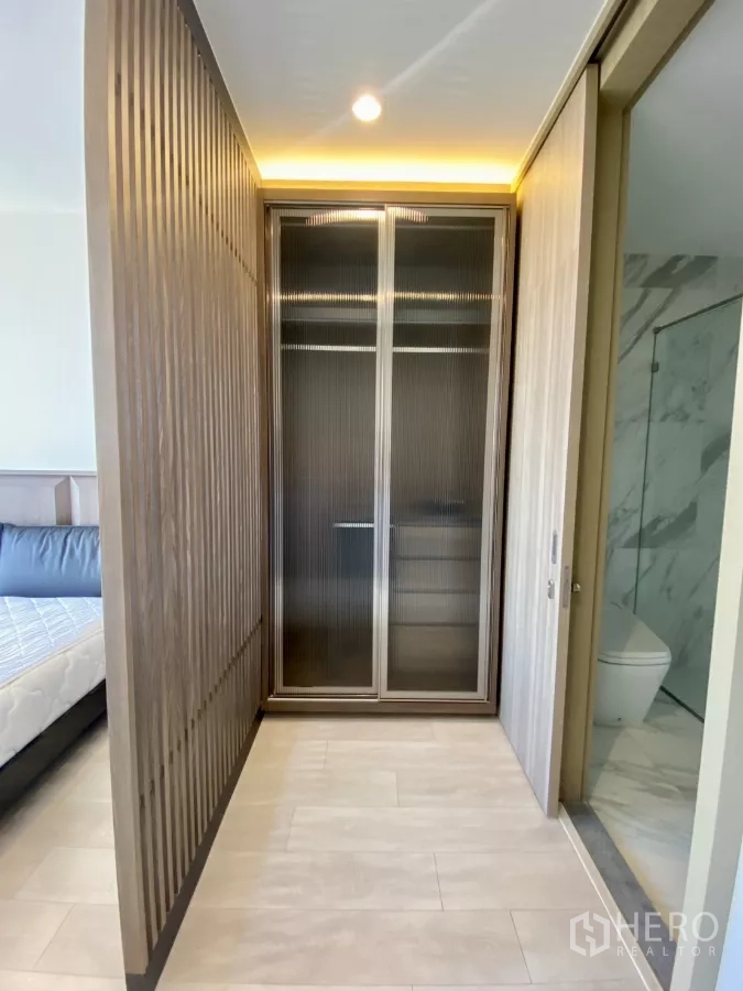 Condominium for sale in Pathum Wan, Bangkok - Walk-in corridor with fluted wood partition, glass-door wardrobe, and access to bathroom.