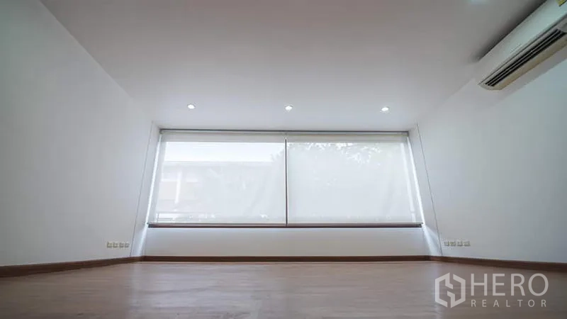 Townhouse for rent or sale in Phra Khanong, Bangkok - Bedroom with a wide window, blackout blinds, wood floors and split-type air conditioner.
