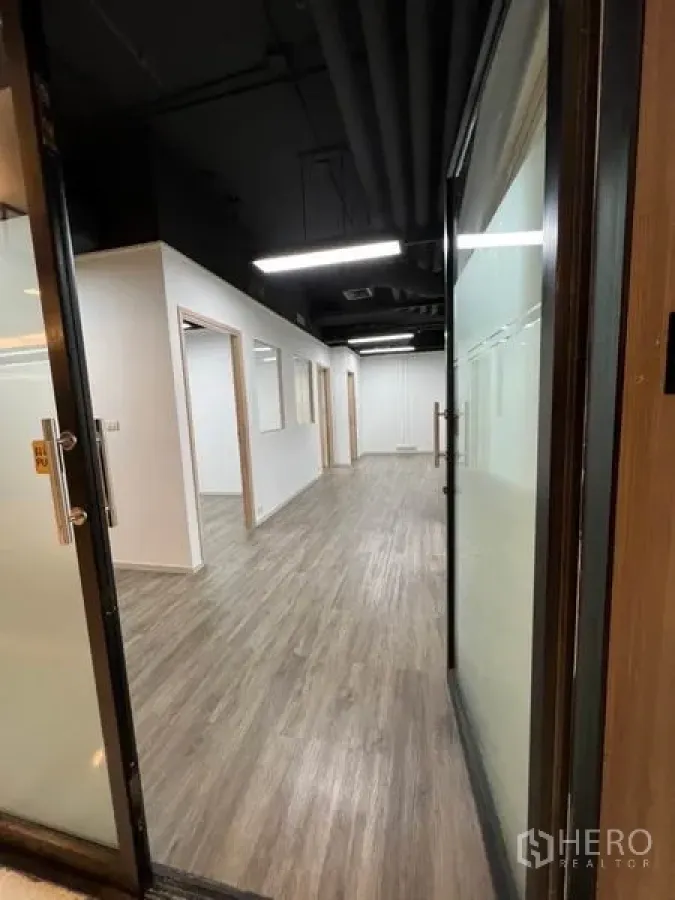 Office Space for rent in Khlong Toei, Bangkok - View through glass doors into modern office corridor with wood floors and black ceiling.