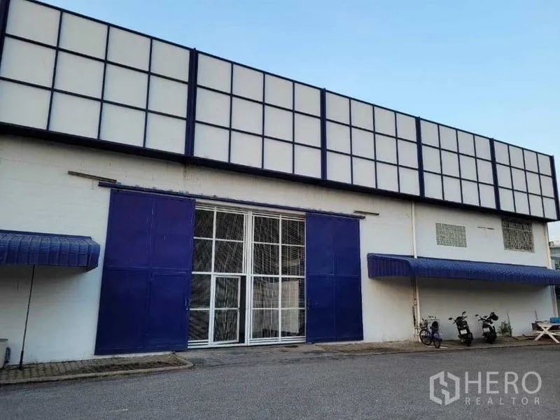Warehouse for rent in Phra Khanong, Bangkok - Front entrance with blue sliding doors and a secure metal gate