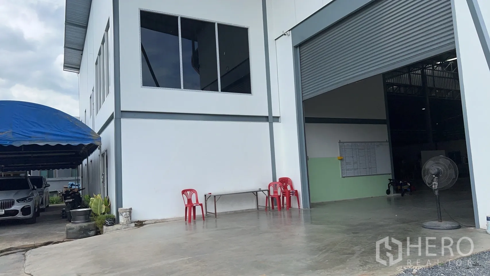Warehouse for sale in Lam Luk Ka, Pathum Thani - Concrete apron at the loading bay with white facade and oversized shutter door.