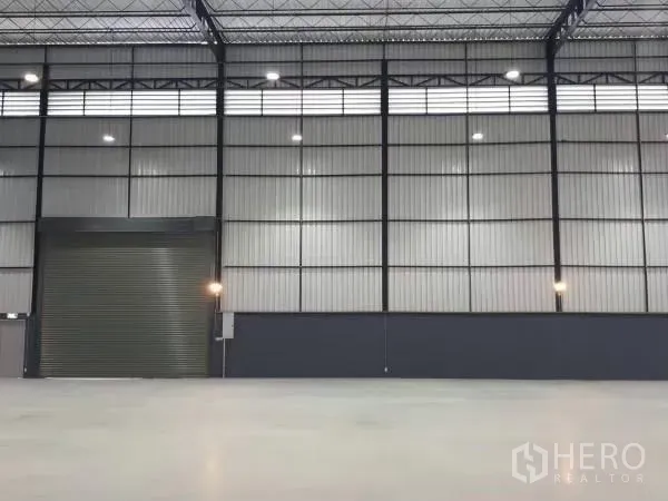 货栈 出租在Khlong Sam Wa, Bangkok - 仓库内部，高金属墙体、大型卷帘门与抛光混凝土地面。