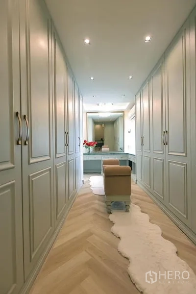 Detached House for rent or sale in Watthana, Bangkok - Walk-in wardrobe corridor with full-height cabinetry, vanity and herringbone wood floor.