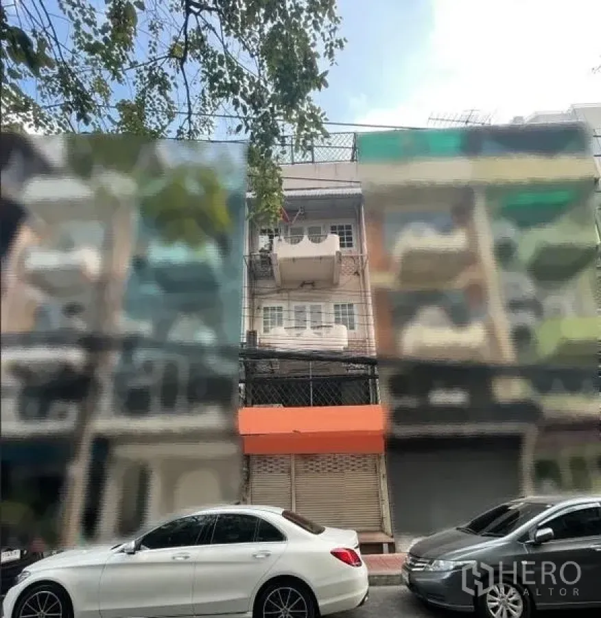 Shophouse for rent in Phaya Thai, Bangkok - Street view of a row of shophouses with parked cars, highlighting the unit with the orange canopy.