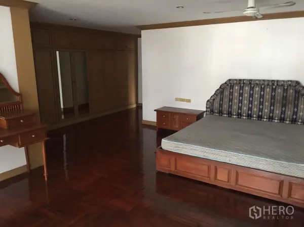 Condominium for rent in Khlong Toei, Bangkok - Bedroom featuring wall-length wardrobes, dressing table, and shiny parquet flooring.