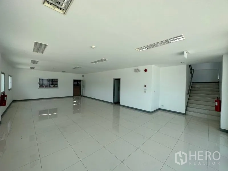 Factory for rent in Mueang Samut Prakan, Samut Prakan - Open-plan office with white walls, tiled floors, ceiling lights and internal staircase.
