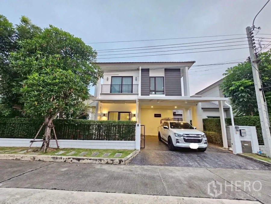 Detached House for sale in Bang Phli, Samut Prakan - Modern two-storey detached house exterior with carport, paved driveway, lawn and hedges on a quiet community street.