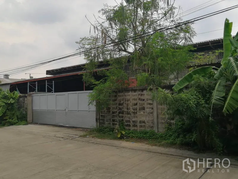 Warehouse for rent in Min Buri, Bangkok - Gated warehouse compound with high brick wall and wide metal sliding gate on a quiet street in Min Buri.