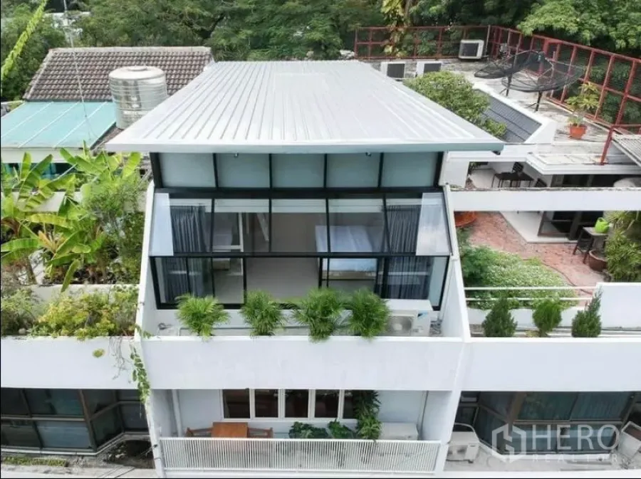 Townhouse for rent in Khlong Toei, Bangkok - Modern multi-level townhouse facade with large glass walls, rooftop and green planters.