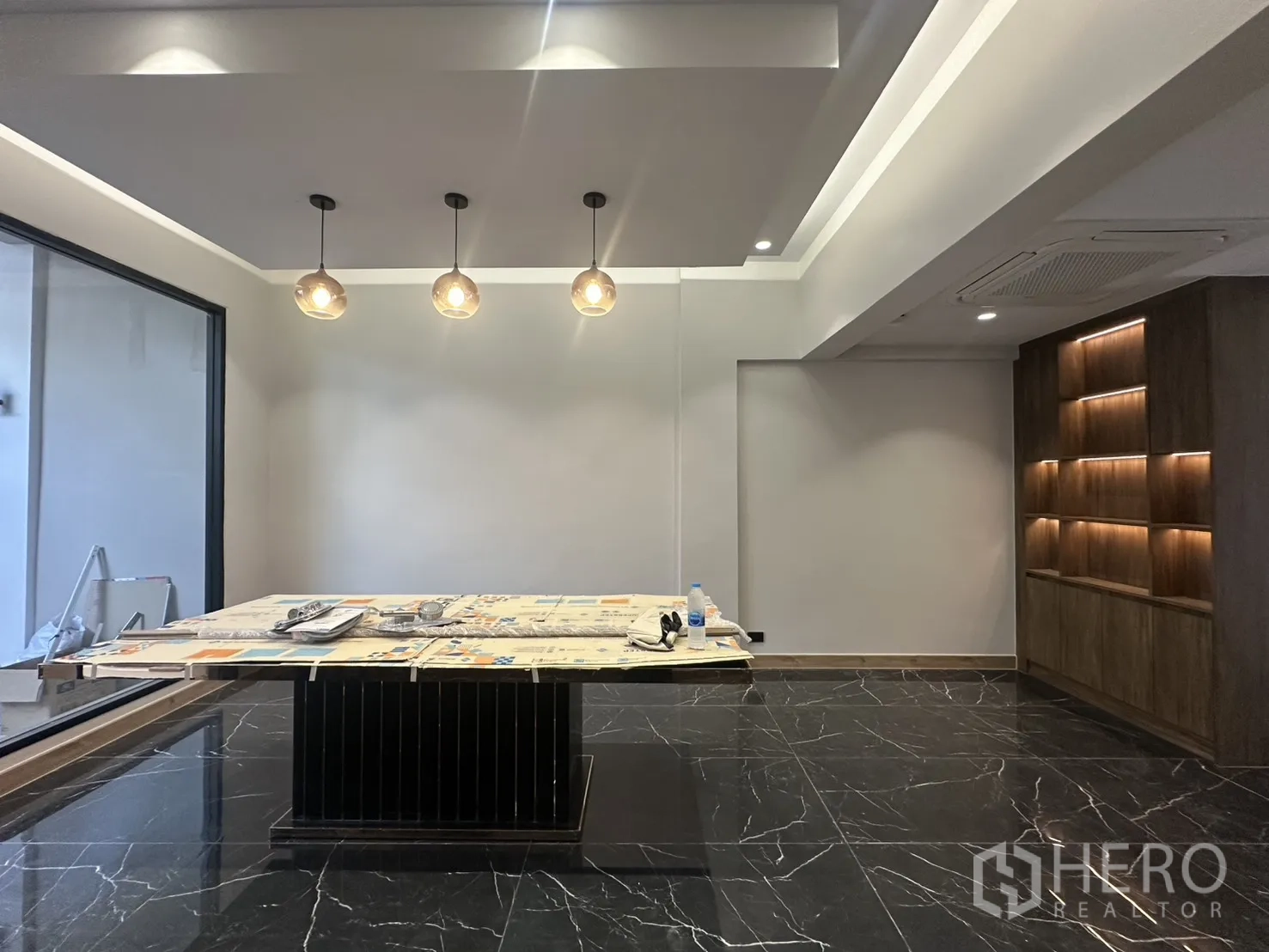 Home Office for rent in Watthana, Bangkok - Room with three pendant lights and a central table next to display shelving.