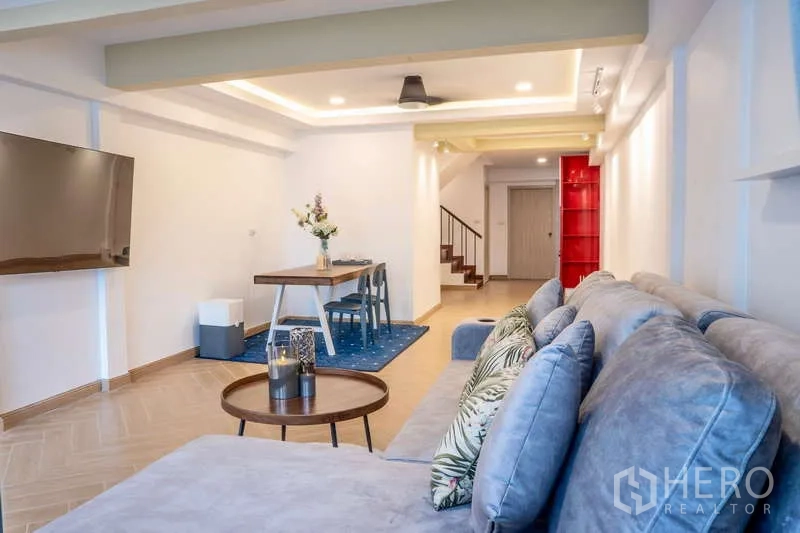 Townhouse for rent in Khlong Toei, Bangkok - Open-plan living and dining area with wall-mounted TV and staircase beyond.