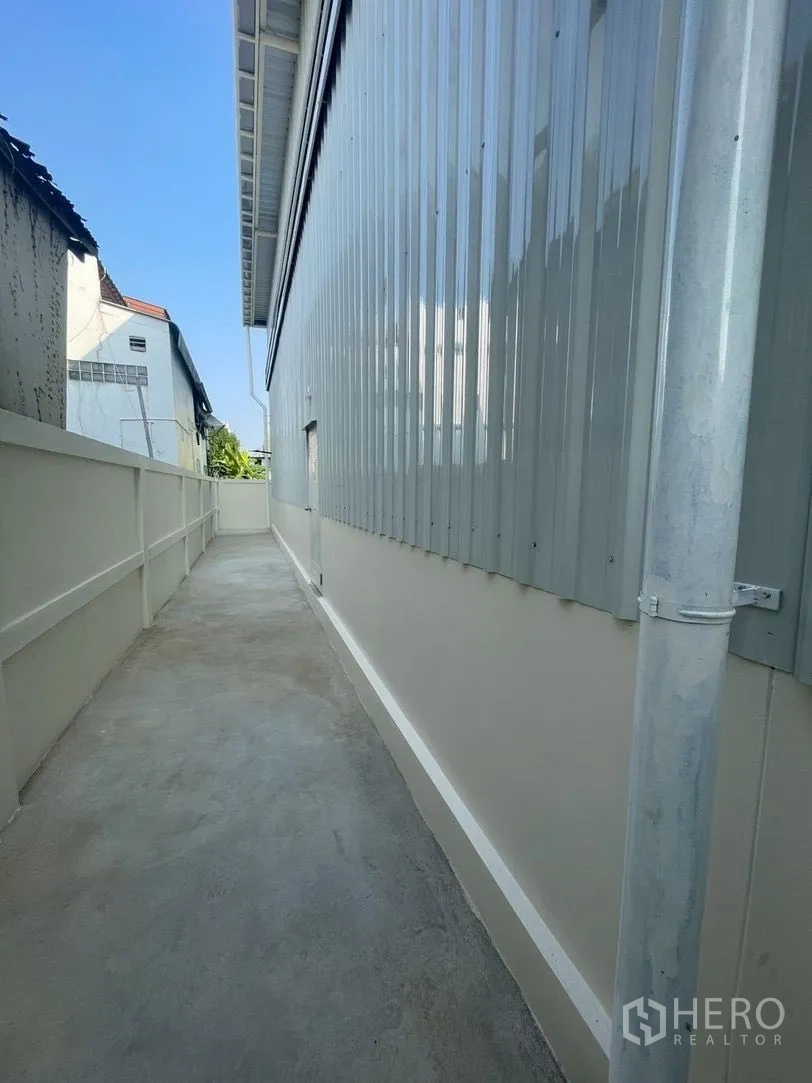 Warehouse for rent in Prawet, Bangkok - Side walkway with a concrete path along a corrugated warehouse wall.