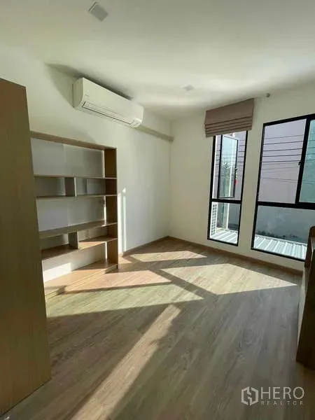 Townhouse for rent or sale in Bang Kapi, Bangkok - Sunlit room with built-in shelving, air conditioner and tall windows.