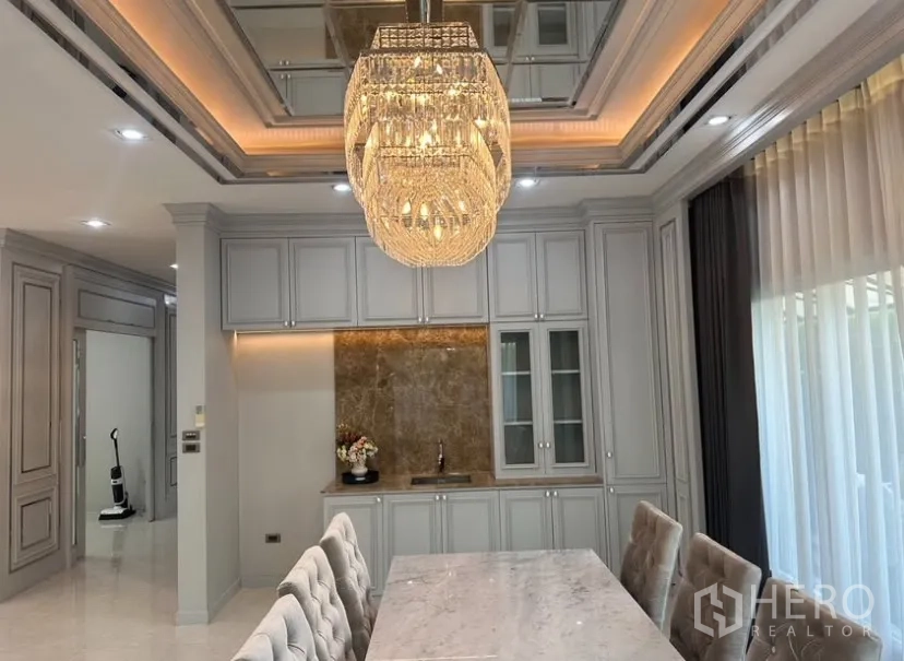 Detached House for rent or sale in Prawet, Bangkok - View of the dining room with statement chandelier, glass-front cabinets, and full-height drapes.