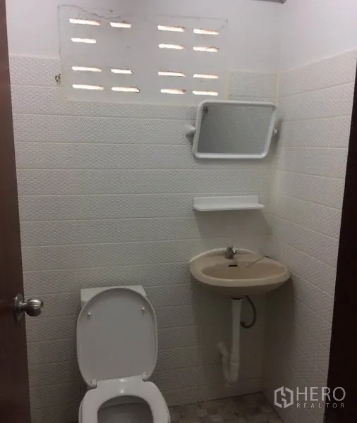 Warehouse for rent in Pathum Thani - Simple tiled restroom with toilet, sink, and ventilation blocks inside the warehouse.