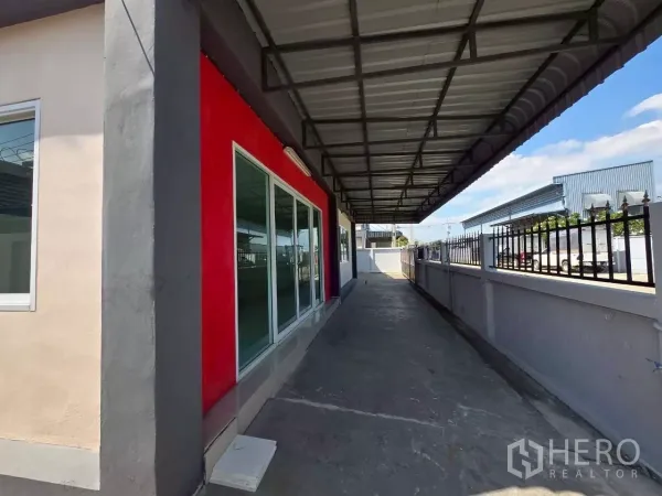 Factory for rent or sale in Mueang Samut Sakhon, Samut Sakhon - Covered side walkway with metal roof along the glass-fronted office and perimeter fence of the factory.