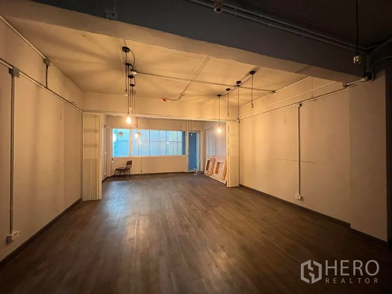Shophouse for rent - Large flexible workspace with window and warm lighting on wood flooring.