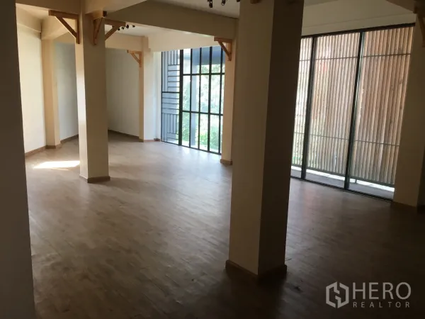Retail Space for rent in Khlong Toei, Bangkok - Bright showroom area with pillars, wood flooring, and floor-to-ceiling windows with vertical slats.