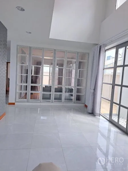Detached House for rent in Prawet, Bangkok - Light-filled living area with white tile floor, glass partition wall and sliding doors.