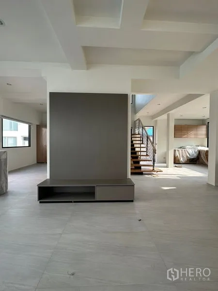 Detached House for rent in Watthana, Bangkok - Spacious living room with feature TV wall, coffered ceiling, and staircase leading to kitchen.