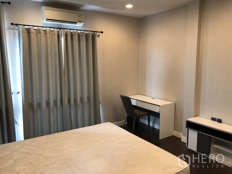 Detached House for rent or sale in Bang Kapi, Bangkok - Bedroom with study desk, full-length curtains and neutral décor.