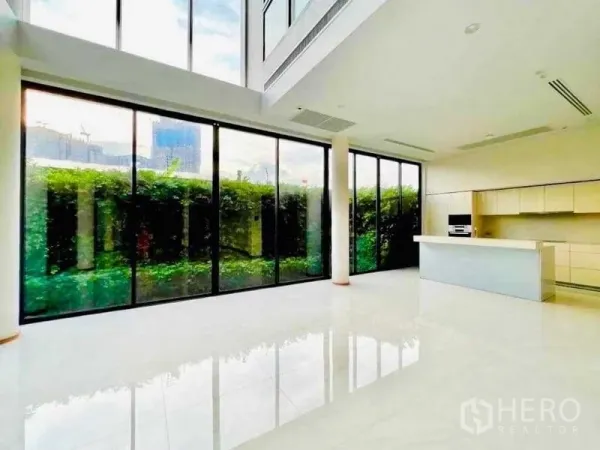 Detached House for sale in Huai Khwang, Bangkok - Bright double-height living area with floor-to-ceiling glass and a modern island kitchen facing a hedged garden.