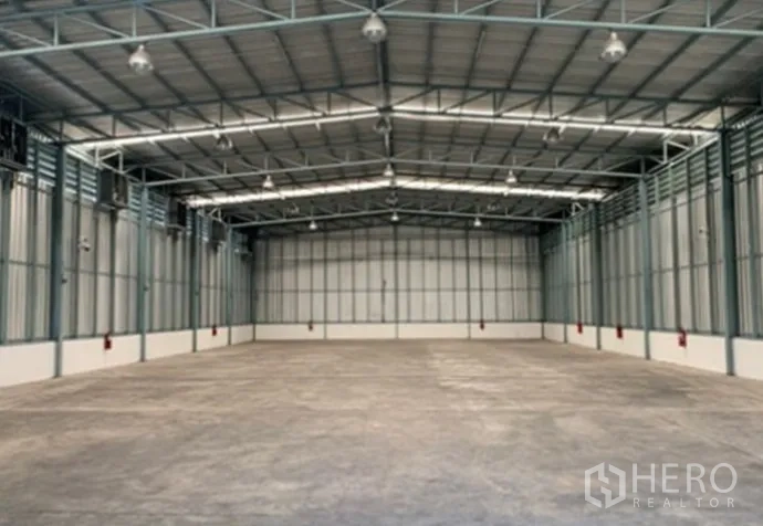 Warehouse for rent in Suan Luang, Bangkok - Spacious empty warehouse interior with high steel truss roof, concrete floor, and bright skylights.